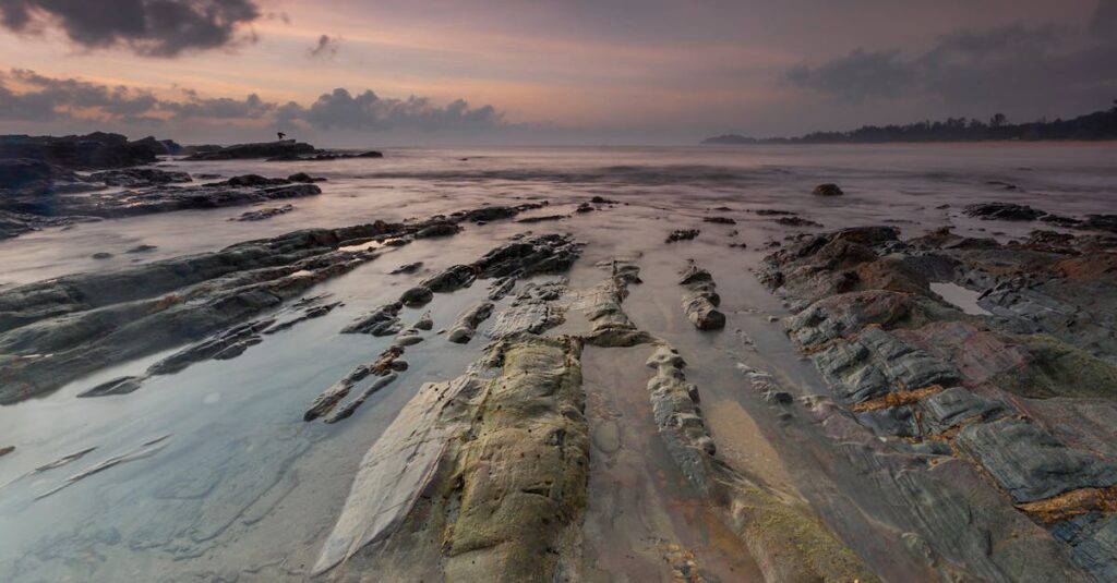 Calm ocean waves over rocky beach at twilight with dramatic sky.