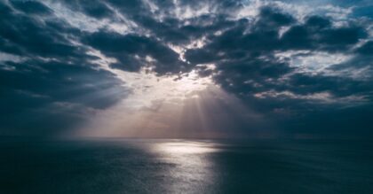 A breathtaking view of the ocean at sunset, with dramatic clouds and sunrays breaking through, creating a serene seascape.
