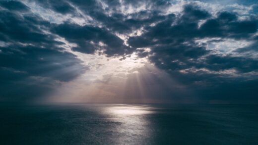 A breathtaking view of the ocean at sunset, with dramatic clouds and sunrays breaking through, creating a serene seascape.